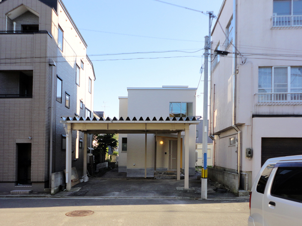 ３階建ての建物に囲まれた土地に建っている住宅と、建て替え前から使っていた鉄骨製の頑丈な車庫